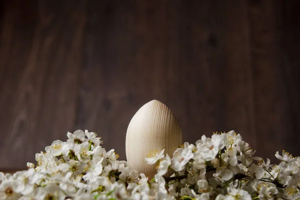 Wooden easter eggs among flowering cherry branches on a rustic table. symbolic composition of the spring holiday for a gift card. copy space. close up. petals of white flowers. the rebirth of nature — Stock Photo, Image