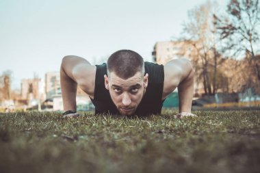 Spor giyimli genç adam stadyumdaki çimlerin üzerinde egzersiz yapıyor. Yerde eğitim görüyor. Şınav çek. şınav