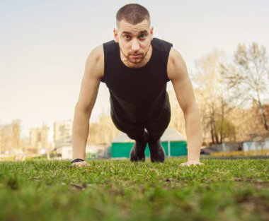 Spor giyimli genç adam stadyumdaki çimlerin üzerinde egzersiz yapıyor. Yerde eğitim görüyor. Şınav çek. şınav
