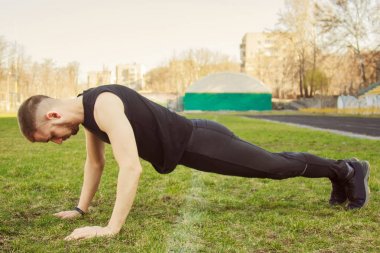 Spor giyimli genç adam stadyumdaki çimlerin üzerinde egzersiz yapıyor. Yerde eğitim görüyor. Şınav çek. şınav