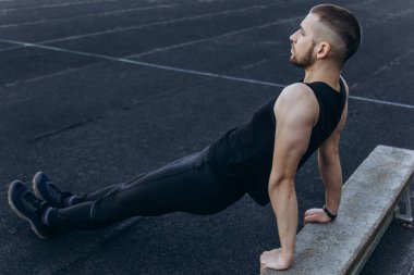 Siyah elbiseli genç bir adam açık havada yakın egzersiz. spor alanında fitness sporcusu. mermi ile eğitim. yaz için vücut hazırlığı ısınmak