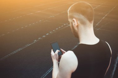 Siyah elbiseli genç bir adam telefona bakıyor. spor alanında fitness sporcusu. gadget'lar ile eğitim. yaz için vücut hazırlık ısınmak. izleme çalıştırma