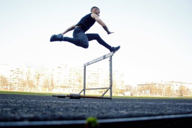 bir bariyerin üzerinden atlayan beyaz bir erkek. stadyumda çalışıyor. Uçuş spor üniforması atletizm koşucusu. enerjik fiziksel aktiviteler. açık hava egzersiz, sağlıklı yaşam tarzı. engelli