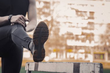 Siyah elbiseli bir adam açık havada bariyerli egzersiz yapmaktır. spor alanında fitness sporcusu. engel ile eğitim. bacaklar germe kadar ısınmak. yaz için vücut hazırlığı