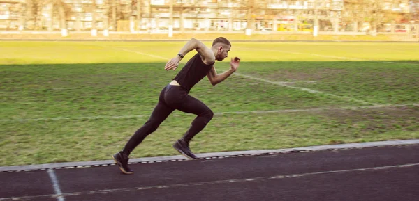 Um homem caucasiano está a fazer um sprint start. correndo no estádio em uma pista de borracha. Pista e corredor de campo em uniforme desportivo. atividades físicas energéticas. exercício ao ar livre, estilo de vida saudável — Fotografia de Stock