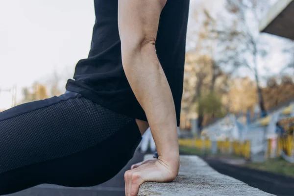 Młody mężczyzna w czarnych ubraniach ćwiczy na świeżym powietrzu z bliska. sportowca fitness na boisku sportowym. Trening z pociskami. Przygotowanie do ogrzania ciała na lato — Zdjęcie stockowe