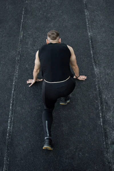 Homem caucasiano a fazer um sprint start. correndo no estádio em uma pista. Pista e corredor de campo em uniforme desportivo. atividades físicas energéticas. exercício ao ar livre, estilo de vida saudável. vista superior vertical — Fotografia de Stock