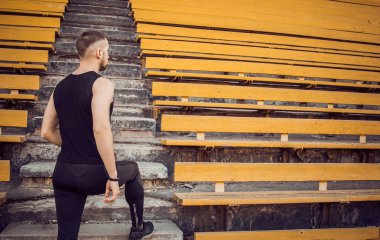 Siyah spor giyimli ince bir genç adam merdiven stadyum standları önünde duruyor. eylem için hazır, zafere adım, meydan okuma