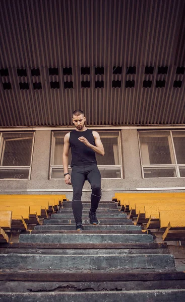 Homem caucasiano treina a correr nas escadas. Pista e corredor de campo no esporte uniforme de treinamento ao ar livre. Atleta, vista de cima. Exercício. Desce. vertical — Fotografia de Stock