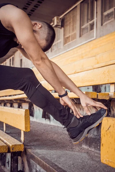 A slender young man in black clothes is exercising outdoors on the stairs. fitness athlete. training with projectiles. warm up body preparation for the summer. stretching up. vertical