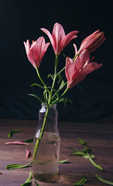 Buquê de flores de lírio rosa nos raios de luz em um fundo preto em uma mesa rústica de madeira em uma garrafa de vidro. botões frescos de uma fábrica florescente close-up em um vaso, espaço de cópia. estúdio tiro — Fotografia de Stock