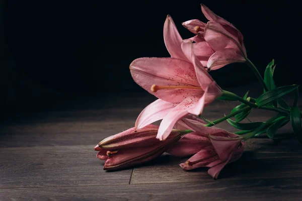 一束粉红色的百合花在光线的光线上，在一个木制的质朴的桌子上的黑色背景。开花植物的新鲜芽特写，复制空间。工作室拍摄。节日贺卡的情节 — 图库照片