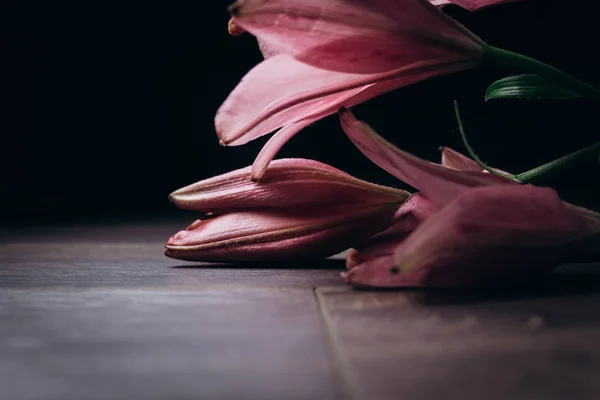 一束粉红色的百合花在光线的光线上，在一个木制的质朴的桌子上的黑色背景。开花植物的新鲜芽特写，复制空间。工作室拍摄。节日贺卡的情节 — 图库照片