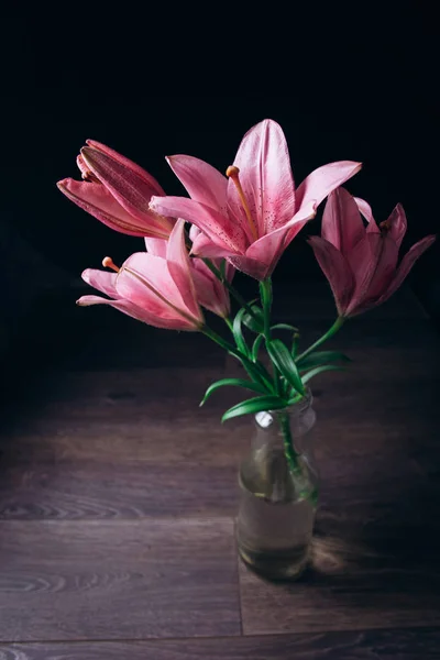 Buquê de flores de lírio rosa nos raios de luz em um fundo preto em uma mesa rústica de madeira em uma garrafa de vidro. botões frescos de uma fábrica florescente close-up em um vaso, espaço de cópia. estúdio tiro — Fotografia de Stock