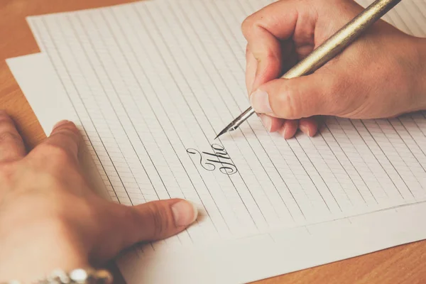 La mano femenina escribe con un bolígrafo de tinta en una hoja de papel blanco con rayas. papelería en escritorio de madera cerca de vista superior. lecciones de ortografía y ejercicios de caligrafía —  Fotos de Stock