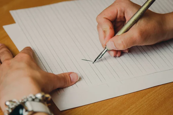 La mano femenina escribe con un bolígrafo de tinta en una hoja de papel blanco con rayas. papelería en escritorio de madera cerca de vista superior. lecciones de ortografía y ejercicios de caligrafía —  Fotos de Stock