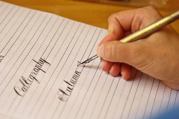 Main féminine écrit avec le stylo encré sur une feuille de papier blanc avec des rayures. papeterie sur bureau vue rapprochée sur le dessus. leçons d'orthographe et exercices de caligraphie. Modèle, disposition, arrière-plan — Photo