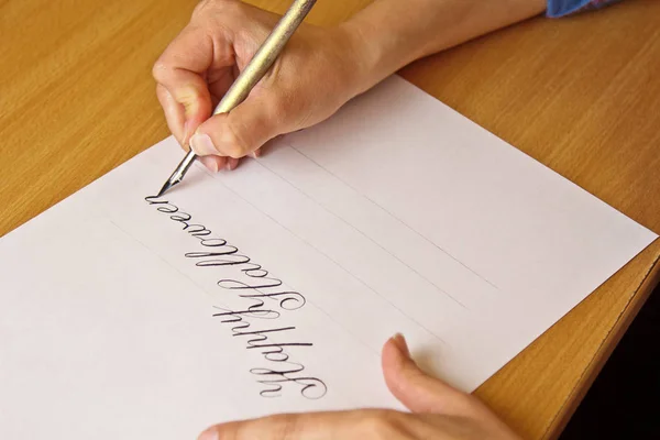 Mano escribe con la pluma de tinta el halloween feliz en una hoja de papel blanco con rayas. papelería en el escritorio de cerca vista superior. lecciones de ortografía y ejercicios de caligrafía. Plantilla, diseño, fondo —  Fotos de Stock