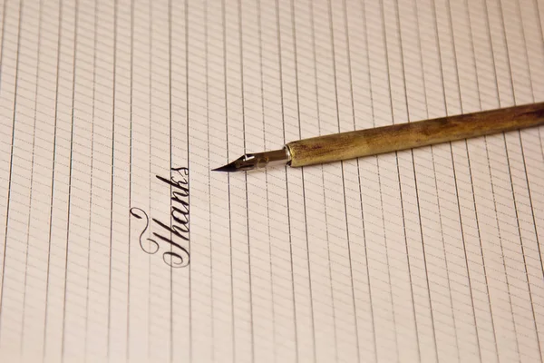 Palabra gracias se escribe con una pluma de tinta de madera en una hoja de papel blanco con rayas dibujadas. papelería de cerca vista superior. lecciones de ortografía y ejercicios de caligrafía. Plantilla, diseño, fondo —  Fotos de Stock