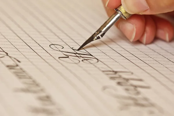 Mão feminina escreve com a caneta de tinta em uma folha de papel branco com listras. artigos de papelaria na mesa de perto vista superior. aulas de ortografia e exercícios de caligrafia. Modelo, layout, fundo. macro — Fotografia de Stock