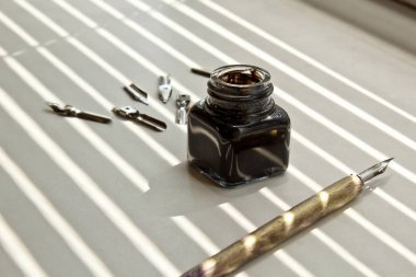 Güneş ışınları beyaz bir arka plan üzerinde mürekkep kalem için metal ipuçları ile Mürekkep Pot. beyaz masada kırtasiye üst görünümü kapatın. yazım dersleri ve kaligrafi egzersizleri. Şablon, düzen, arka plan