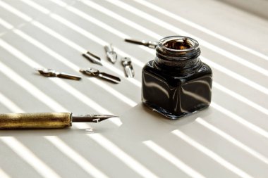 Güneş ışınları beyaz bir arka plan üzerinde mürekkep kalem için metal ipuçları ile Mürekkep Pot. beyaz masada kırtasiye üst görünümü kapatın. yazım dersleri ve kaligrafi egzersizleri. Şablon, düzen, arka plan