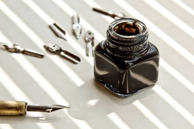 Güneş ışınları beyaz bir arka plan üzerinde mürekkep kalem için metal ipuçları ile Mürekkep Pot. beyaz masada kırtasiye üst görünümü kapatın. yazım dersleri ve kaligrafi egzersizleri. Şablon, düzen, arka plan