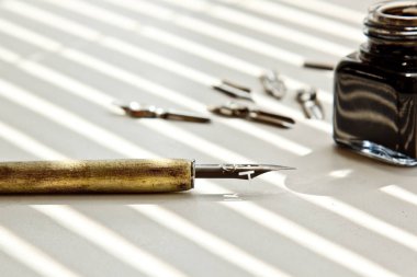 Güneş ışınları beyaz bir arka plan üzerinde mürekkep kalem için metal ipuçları ile Mürekkep Pot. beyaz masada kırtasiye üst görünümü kapatın. yazım dersleri ve kaligrafi egzersizleri. Şablon, düzen, arka plan