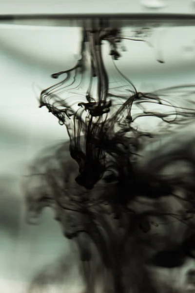 Eine Wolke Tinte in einem transparenten Glasbecher mit klarem Wasser vor dem Hintergrund eines gestreiften Bildschirms mit Lichtstrahlen. Vorlage, Layout, Hintergrund, Textur. Makrodiffusion schwarz-weiß — Stockfoto