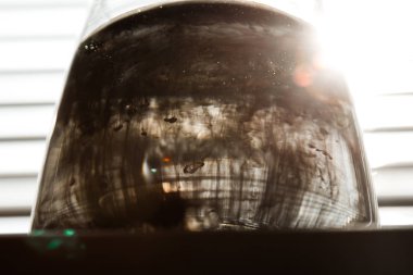 ışık ışınları ile çizgili bir ekranın arka planında açık su ile şeffaf bir cam bardak mürekkep bulutu. Şablon, düzen, arka plan, doku. makro difüzyon siyah beyaz