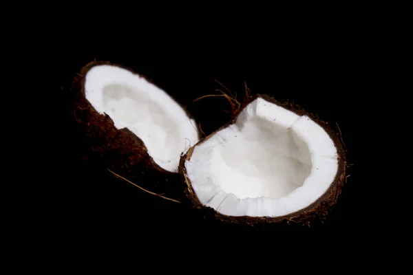 Dojrzały orzech kokosowy jest podzielony na dwie połówki izolowane na czarnym tle zbliżenie. z wnętrza tropikalnego płód dłoni — Zdjęcie stockowe