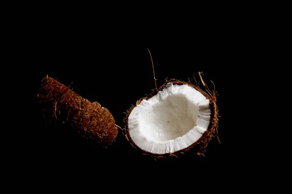 Спелый кокос разбивается на две половинки, изолированные на черном фоне крупным планом. внутренности тропического пальмового плода — стоковое фото