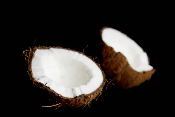 Noix de coco mûre est brisée en deux moitiés isolées sur un fond noir gros plan. l'intérieur du foetus de palmier tropical — Photo