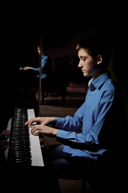 Genç adam piyanonun başında oturuyor. Erkek çocuk müzik okulunda klavye enstrümanı çalıyor. Öğrenci çalmayı öğreniyor. Eller piyanist. Siyah siyah arka plan. dikey