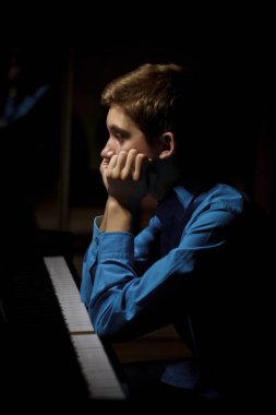 Genç adam piyanonun başında oturuyor. Çocuk müzik okulunda klavye enstrümanını nasıl çaldığını merak ediyordu. Öğrenci çalmayı öğreniyor. Eller piyanist. Siyah siyah arka plan. dikey