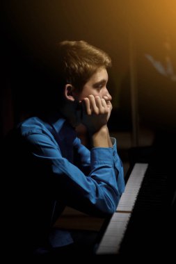 Genç adam piyanonun başında oturuyor. Çocuk müzik okulunda klavye enstrümanını nasıl çaldığını merak ediyordu. Öğrenci çalmayı öğreniyor. Eller piyanist. Siyah siyah arka plan. dikey