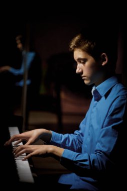 Genç adam piyanonun başında oturuyor. Erkek çocuk müzik okulunda klavye enstrümanı çalıyor. Öğrenci çalmayı öğreniyor. Eller piyanist. Siyah siyah arka plan. dikey