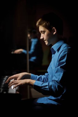 Genç adam piyanonun başında oturuyor. Erkek çocuk müzik okulunda klavye enstrümanı çalıyor. Öğrenci çalmayı öğreniyor. Eller piyanist. Siyah siyah arka plan. dikey