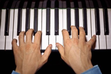 Piyanoda iki erkek eli. avuç içi tuşları üzerinde yalan ve müzik okulunda klavye liç. öğrenci oynamayı öğrenir. eller piyanist. siyah koyu arka plan. üst görünüm