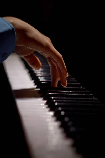 Una mano maschile al pianoforte. Il palmo poggia sui tasti e suona lo strumento a tastiera nella scuola di musica. studente impara a giocare. pianista mani. sfondo nero scuro. verticale — Foto Stock