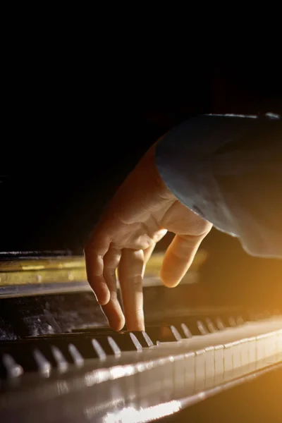 Una mano maschile al pianoforte. Il palmo poggia sui tasti e suona lo strumento a tastiera nella scuola di musica. studente impara a giocare. pianista mani. sfondo nero scuro. verticale — Foto Stock