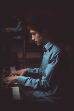 Genç adam piyanonun başında oturuyor. Erkek çocuk müzik okulunda klavye enstrümanı çalıyor. Öğrenci çalmayı öğreniyor. Eller piyanist. Siyah siyah arka plan. dikey