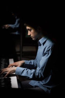 Genç adam piyanonun başında oturuyor. Erkek çocuk müzik okulunda klavye enstrümanı çalıyor. Öğrenci çalmayı öğreniyor. Eller piyanist. Siyah siyah arka plan. dikey