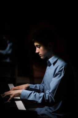 Genç adam piyanonun başında oturuyor. Erkek çocuk müzik okulunda klavye enstrümanı çalıyor. Öğrenci çalmayı öğreniyor. Eller piyanist. Siyah siyah arka plan. dikey
