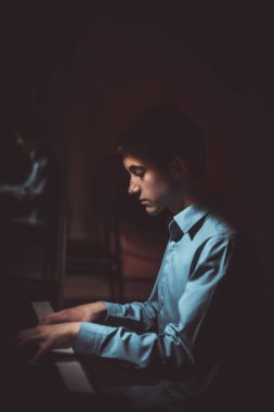 Genç adam piyanonun başında oturuyor. Erkek çocuk müzik okulunda klavye enstrümanı çalıyor. Öğrenci çalmayı öğreniyor. Eller piyanist. Siyah siyah arka plan. dikey