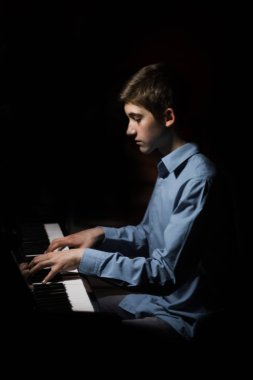 Genç adam piyanonun başında oturuyor. Erkek çocuk müzik okulunda klavye enstrümanı çalıyor. Öğrenci çalmayı öğreniyor. Eller piyanist. Siyah siyah arka plan. dikey