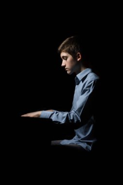 Genç adam piyanonun başında oturuyor. Erkek çocuk müzik okulunda klavye enstrümanı çalıyor. Öğrenci çalmayı öğreniyor. Eller piyanist. Siyah siyah arka plan. dikey