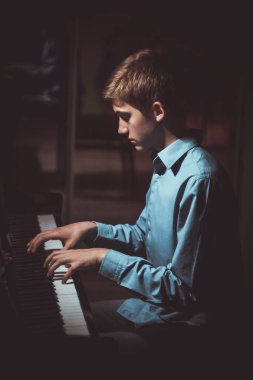 Genç adam piyanonun başında oturuyor. Erkek çocuk müzik okulunda klavye enstrümanı çalıyor. Öğrenci çalmayı öğreniyor. Eller piyanist. Siyah siyah arka plan. dikey