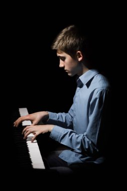 Genç adam piyanonun başında oturuyor. Erkek çocuk müzik okulunda klavye enstrümanı çalıyor. Öğrenci çalmayı öğreniyor. Eller piyanist. Siyah siyah arka plan. dikey