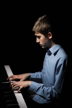 Genç adam piyanonun başında oturuyor. Erkek çocuk müzik okulunda klavye enstrümanı çalıyor. Öğrenci çalmayı öğreniyor. Eller piyanist. Siyah siyah arka plan. dikey